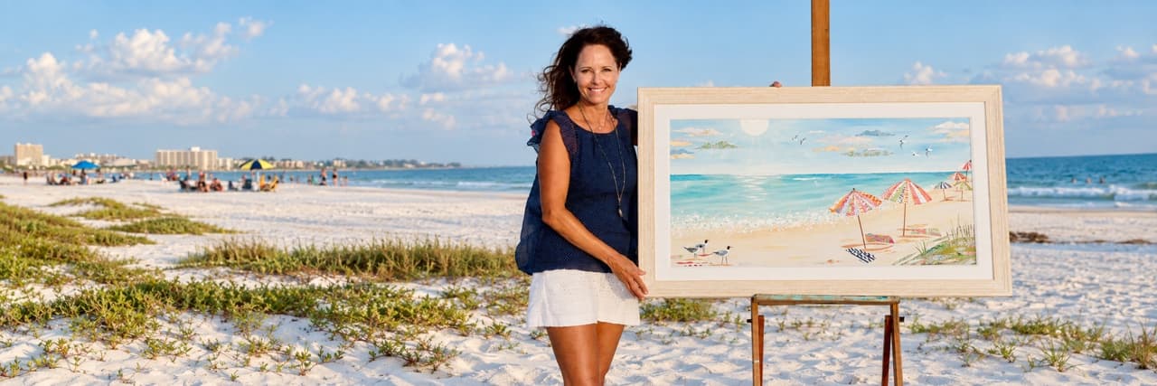 Jennifer Peck on a Florida beach beside a framed beach painting on an easel