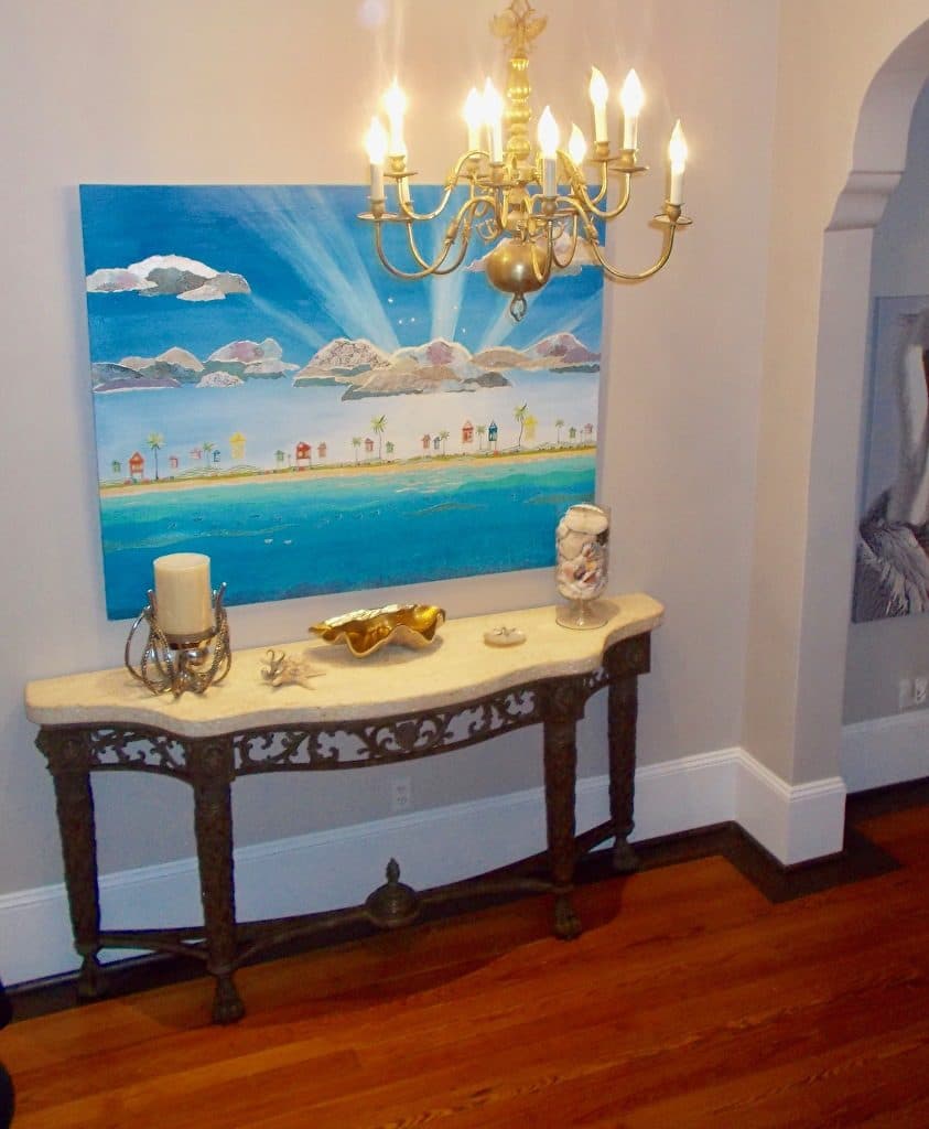 A beach-town collage over a marble-topped console under a chandelier