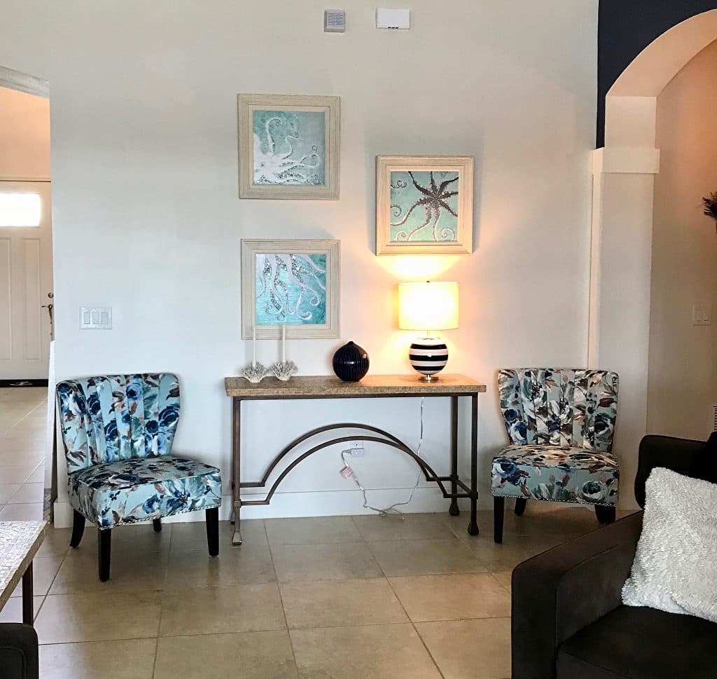 Three framed sea-life prints above a console table between two patterned chairs