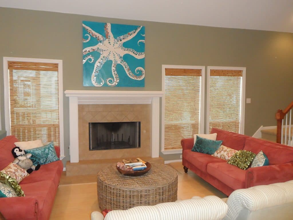 A turquoise octopus collage above a fireplace, between two coral sofas