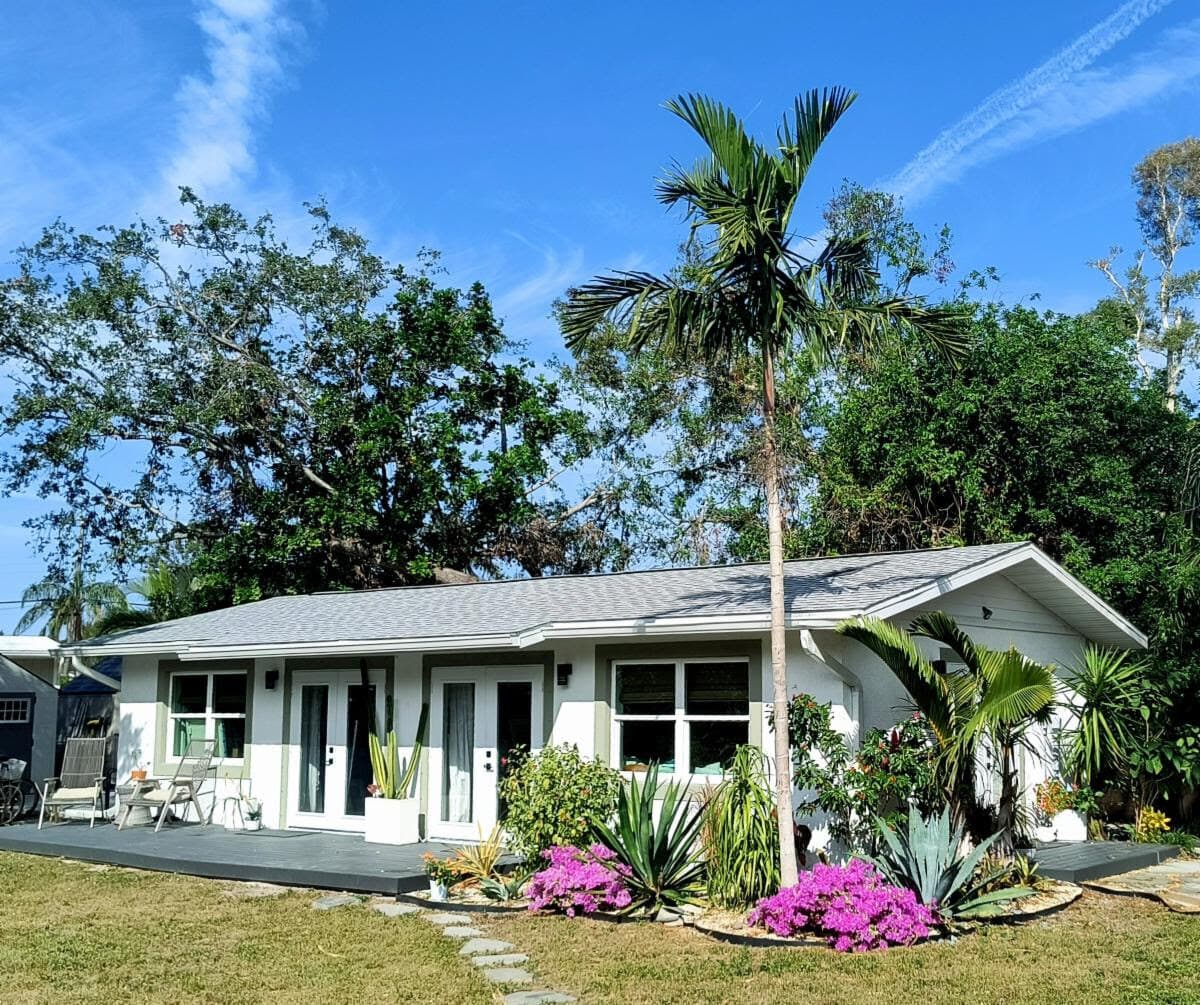 The white studio cottage behind the house, framed by palms and pink flowers