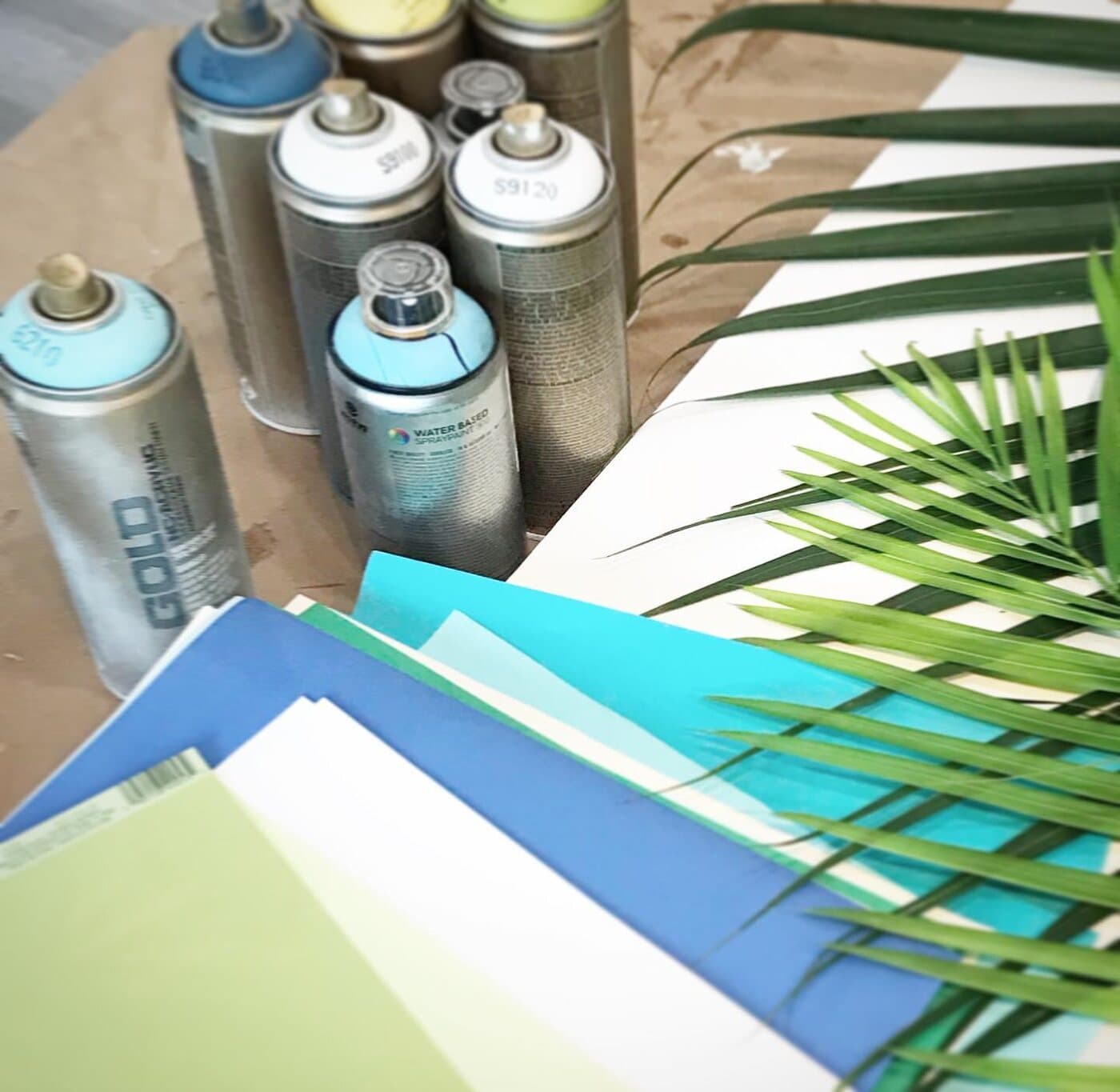 Spray paint cans, palm fronds, and stacks of colored paper on the worktable