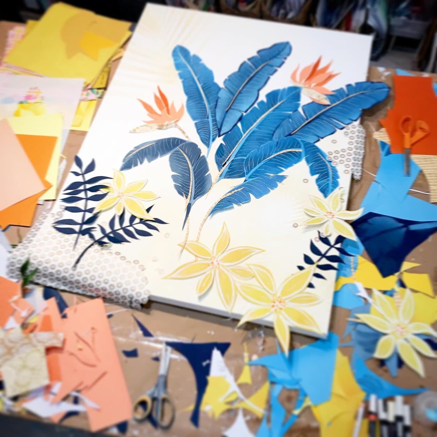 A canvas in progress surrounded by loose cut-paper leaves and flowers