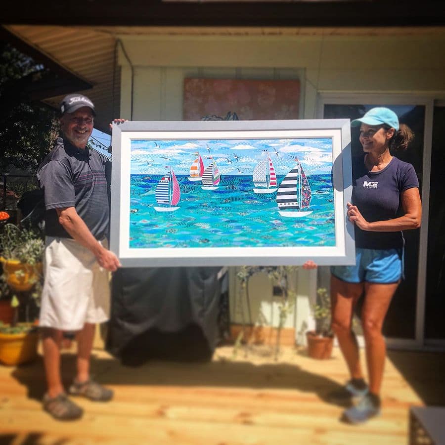 A couple on their porch holding a wide framed sailboat piece