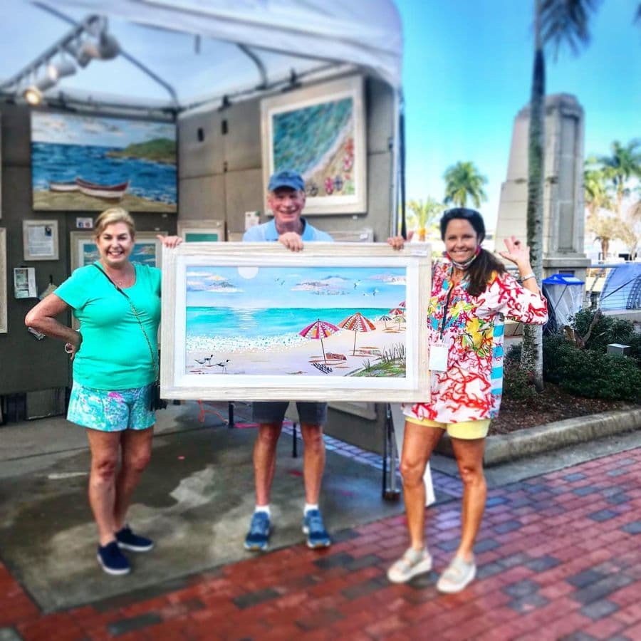 Jennifer and two collectors with a framed beach-umbrella piece outside the tent