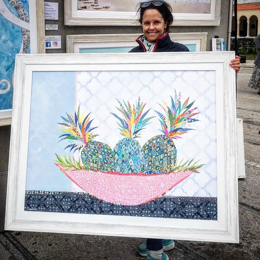 Jennifer holding a wide framed pineapple-bowl collage outside the tent