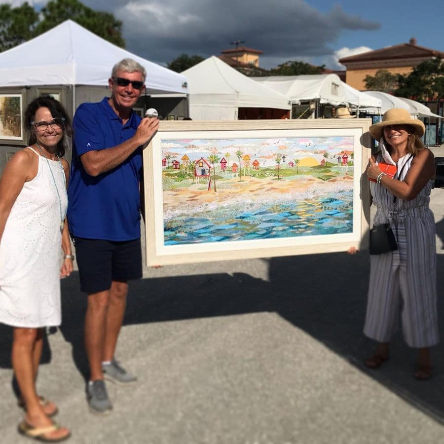 A couple carrying a wide framed beach-houses piece through the show