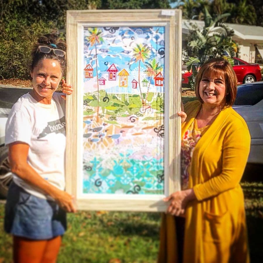 Two collectors holding a tall framed beach-houses piece beside the car