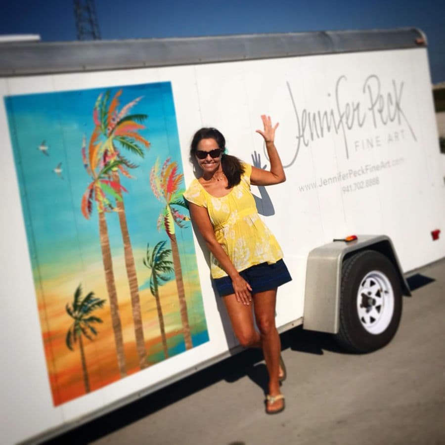 Jennifer waving beside the art trailer, palms painted on its side